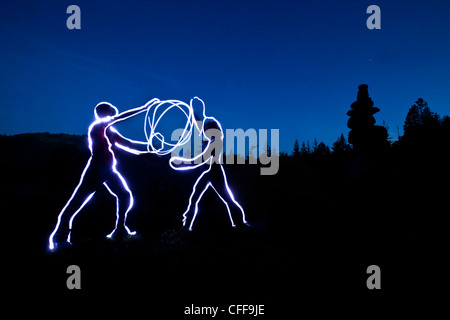 Una pittura di luce di due figure tenendo una palla di energia luminosa al tramonto in Idaho. Foto Stock