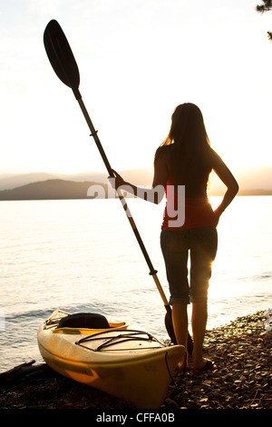 Una giovane e bella donna si rilassa su una spiaggia dopo il kayak al tramonto su un lago in Idaho. Foto Stock