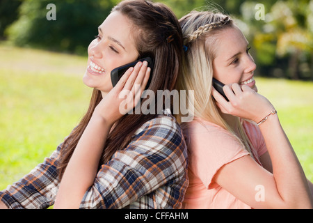 Giovani donne sorridente in piedi di schiena mentre utilizzando i loro telefoni cellulari Foto Stock