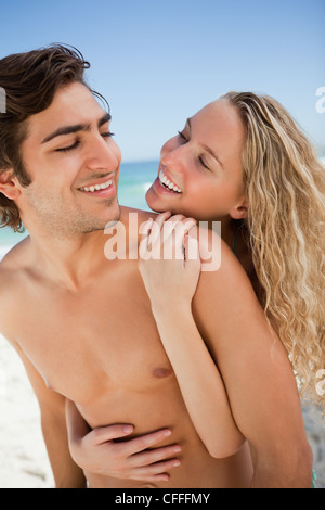 Coppia giovane sorridere mentre abbracciando ogni altro sulla spiaggia Foto Stock