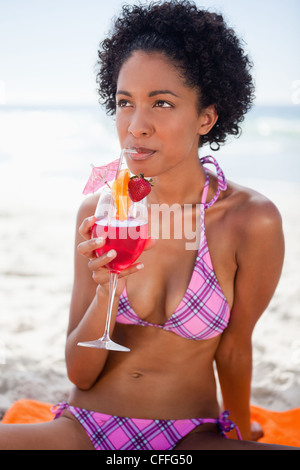 Giovane donna attraente seduto sulla spiaggia bevendo un cocktail di frutta Foto Stock