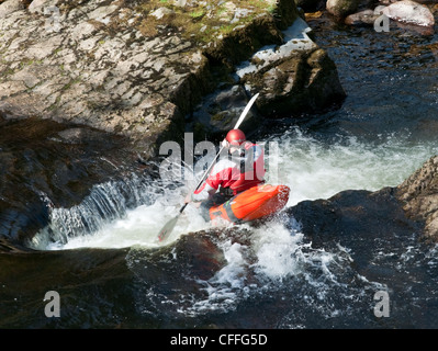 Un colpo lungo di un Kayaker sul fiume andando verso il basso una piccola caduta. Foto Stock