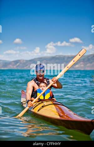 Un uomo pagaie in legno kayak con un 3 anno vecchio ragazzo seduto sul suo giro Bear Lake. Foto Stock