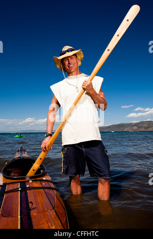 Un uomo che indossa un cappello di paglia come egli si pone per un ritratto con un kayak in legno e la pala che ha fatto mentre in piedi sulla riva di essere Foto Stock