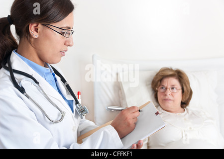 Medico permanente scrive di prescrizione medica per Senior paziente sdraiato a letto Foto Stock