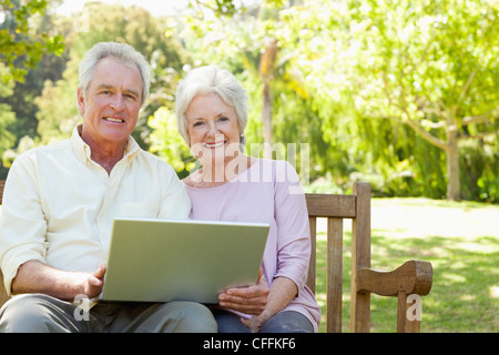 Due amici guardando avanti come siano in possesso di un computer portatile mentre è seduto su una panchina Foto Stock