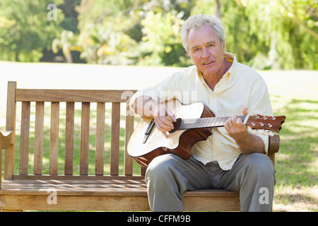 L'uomo guarda avanti durante la riproduzione di una chitarra come egli siede su un banco di lavoro Foto Stock