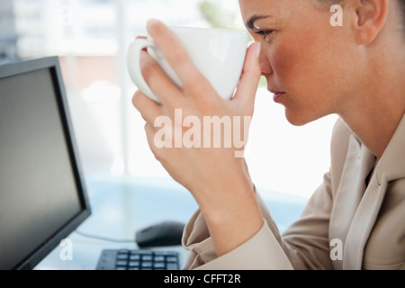 Close-up of a woman taking a mug while looking her screen Foto Stock