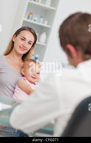 Madre sorridente mentre tiene il suo bambino che sta guardando il medico Foto Stock