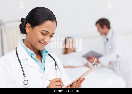 Sorridente medico iscritto sul suo clipboard mentre in piedi in una stanza di ospedale Foto Stock