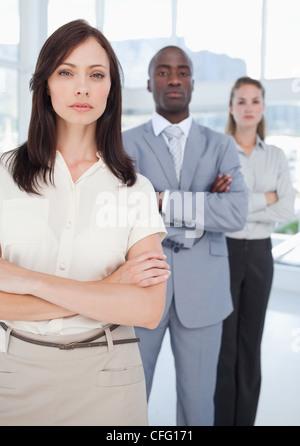 Donna con i suoi due colleghi in piedi dietro di lei con le braccia incrociate Foto Stock
