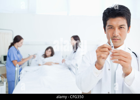 Medico guardando avanti come egli prepara una siringa mentre i suoi colleghi il trattamento di un paziente Foto Stock