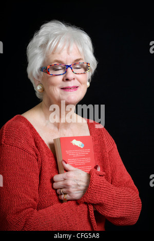 Attraente dama senior azienda prenota nel profondo pensiero dando concetto di ricordando prese contro uno sfondo nero Foto Stock