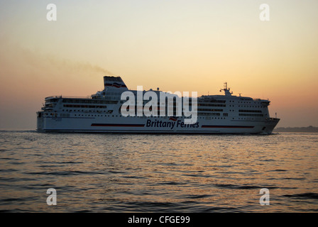 Un canale trasversale traghetto arriva a Portsmouth a seguito di una barca a vela dalla Francia al tramonto. Foto Stock