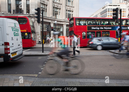 Un ciclista il pendolarismo per lavorare a Londra circondato da autobus rossi Foto Stock