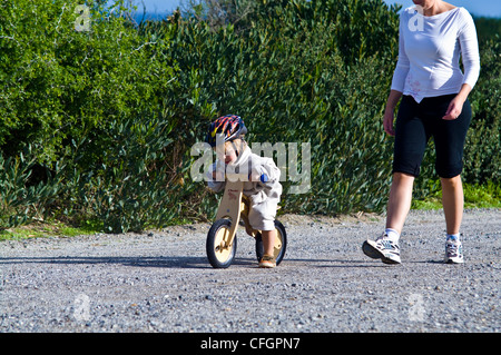 Un giovane ragazzo impara a guidare una moto di equilibrio realizzato dal legno riciclato. Foto Stock