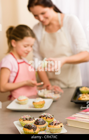 Bambina gusto spruzza come decorare le tortine con la madre a casa Foto Stock