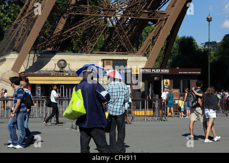 Strada dei venditori di souvenir indossando cappelli ombrelli ai piedi della Torre Eiffel a Parigi Francia Foto Stock