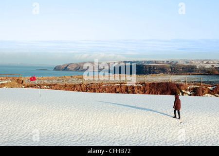 Bambino su una coperta di neve golf in irlanda in inverno con il mare e le scogliere in background Foto Stock