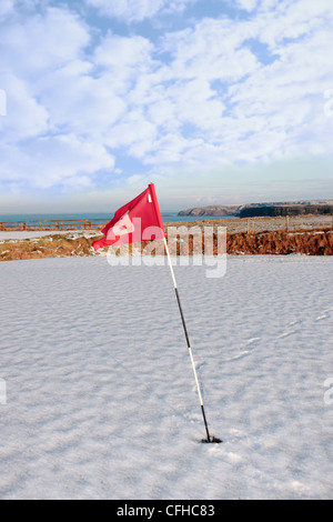 Bandiera su una coperta di neve golf in irlanda in inverno con il mare e le scogliere in background Foto Stock