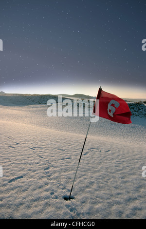 Bandiera su una coperta di neve del campo da golf links di notte in Irlanda in inverno Foto Stock