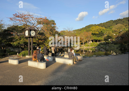 Il popolo giapponese seduti sulle panchine di pietra accanto ad un laghetto in Maruyama Koen park, Kyoto, Giappone Foto Stock