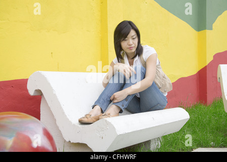 Giovane donna seduta su una panchina Foto Stock