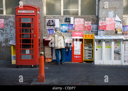 La gente di raccolta e libera lettura giornali cinesi da un edicola in Chinatown, Londra Foto Stock