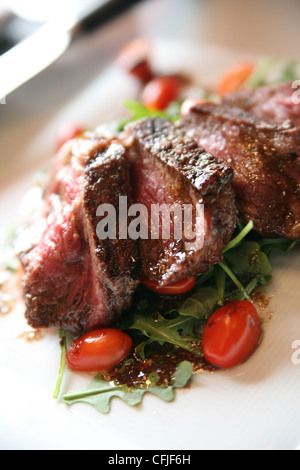 Grigliata di New York Strip bistecca su un letto di foglie di rucola (razzo) con fette di pomodori a pera Foto Stock