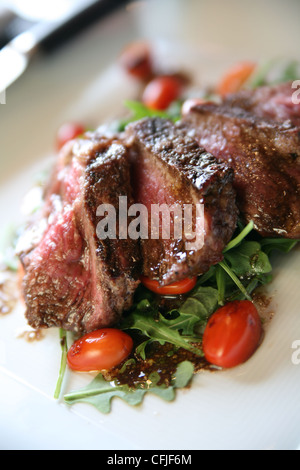 Grigliata di New York Strip bistecca su un letto di foglie di rucola (razzo) con fette di pomodori a pera Foto Stock