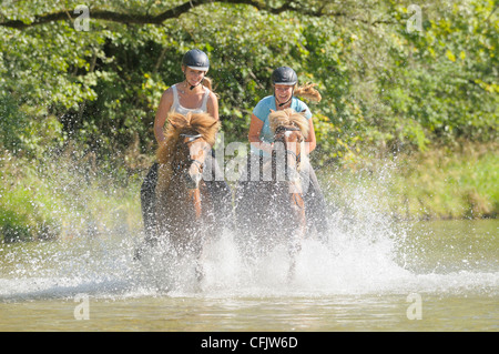 Due giovani piloti sul retro del islandese di cavalli al galoppo nel fiume Isar a sud di Monaco di Baviera, Germania Foto Stock