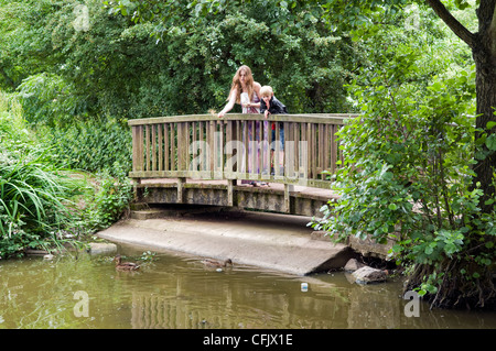 La donna caucasica con 8 anno vecchio ragazzo caucasico alimentando le anatre bastarde a barre corte Moat stagno, vicino Longwell verde in Bristol, Regno Unito Foto Stock