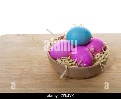Una piccola ciotola di legno riempita con uova colorate e paglia seduti su un tavolo Foto Stock