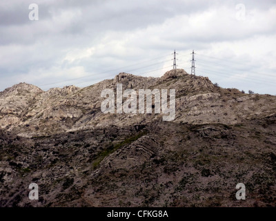 Due lontano elecrical pilones sulla cima di una montagna rocciosa da nuvoloso meteo Foto Stock