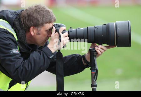 Una pressa fotografo guarda attraverso il mirino mentre a fotografare un evento sportivo. Foto di James Boardman. Foto Stock