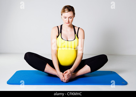 Donna incinta di eseguire uno Stretching interno coscia della gamba tratto su un tappetino Foto Stock