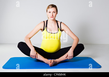 Donna incinta di eseguire uno Stretching interno coscia della gamba tratto su un tappetino Foto Stock