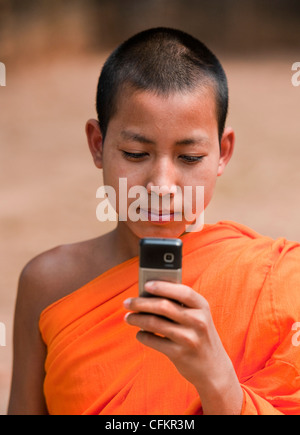 Il debuttante monaco buddista in veste di zafferano dal paese vicino al fiume Mekong, il Laos con un telefono mobile Foto Stock