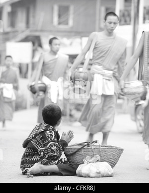 Ragazzo giovane mendicante di cibo dai monaci che hanno ricevuto cibo al daily alms cerimonia di consegna a Luang Prabang, Laos Foto Stock