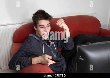 Giovane uomo di guardare la tv da soli, tifo e punzonatura l'aria celebrando. Foto Stock