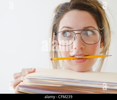 Ritratto di giovane donna che indossa gli occhiali e tenendo premuto matita in bocca, studio shot Foto Stock