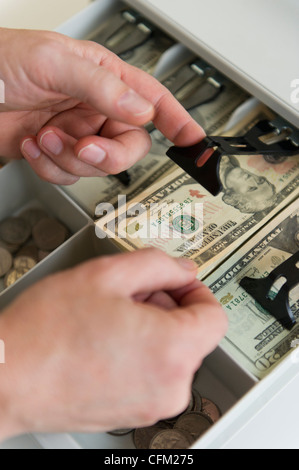 Stretta di mano d'uomo mettendo banconote nel registratore di cassa, studio shot Foto Stock