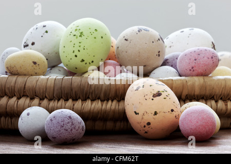Still Life foto di screziato candy ricoperte di cioccolato uova di pasqua in un cesto di vimini su una tavola in legno rustico. Foto Stock