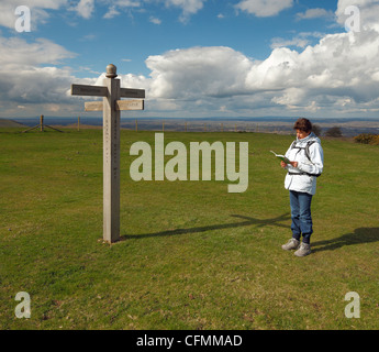 La donna la lettura di una mappa accanto a un faro Ditchling signpost. Foto Stock