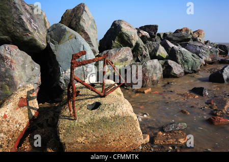 Un vecchio arrugginito telaio di bicicletta dietro la corazza di roccia mare difese a Happisburgh, Norfolk, Inghilterra, Regno Unito. Foto Stock