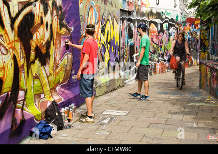 Vista orizzontale di Graffiti Vicolo Werregaran Straat a Gand, con due artisti verniciatura a spruzzo la loro arte sul marciapiede parete. Foto Stock