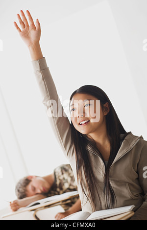 Stati Uniti, California, Los Angeles, Felice schoolgirl rising mano in aula mentre il suo collega dorme sulla sua scrivania Foto Stock