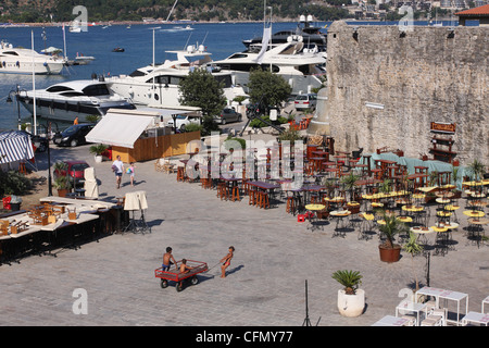 Un bambino tira una carriola sulla piazza vicino le mura della città vecchia. Notte caffè sono vuoti durante il giorno. Budva. Montenegro Foto Stock