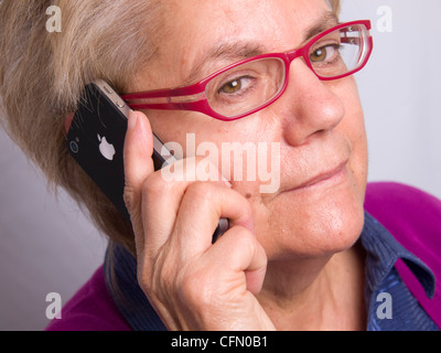 Close up di donna matura con bicchieri rossi parlando su iPhone e guardando la fotocamera Foto Stock