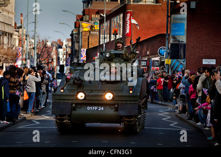 Truppe in veicoli blindati guidare passato High street negozi durante un Yeomanry Royal Parade, spettatori guarda dal marciapiede Foto Stock